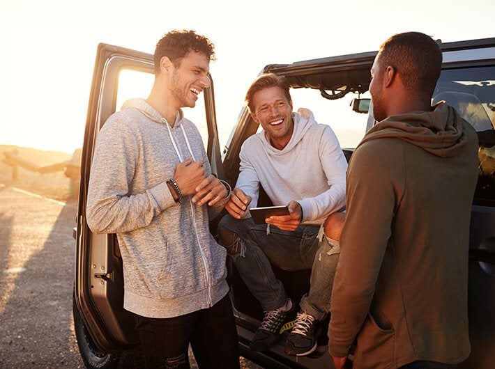 Men's health - 3 men talking with each other next to a car.